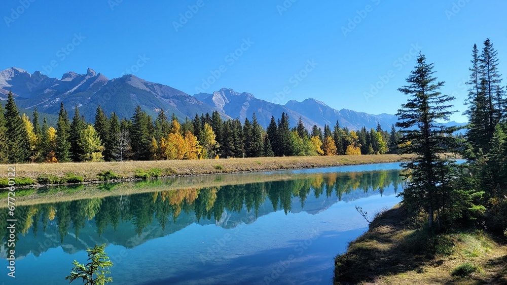 Landscape view of the fir forest trees and mountains reflected i lake against a blue sky