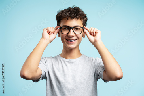 Portrait of smiling teenage boy wearing casual clothes, adjusting eyeglasses, looking at camera © Maria Vitkovska
