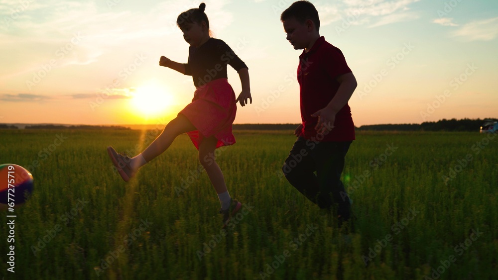 Children run after ball on green grass. Happy family, children at sunset in park play football together. Happy kids playing with ball in park. Children team. Sport Group kids in nature playing ball