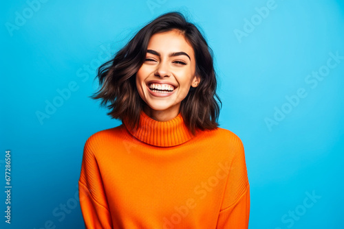 Jeune femme souriante portant un pull orange devant un fond bleu