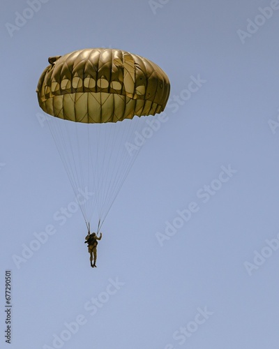 Vertical aerial view of a man flying on a yellow parachute in blue sky