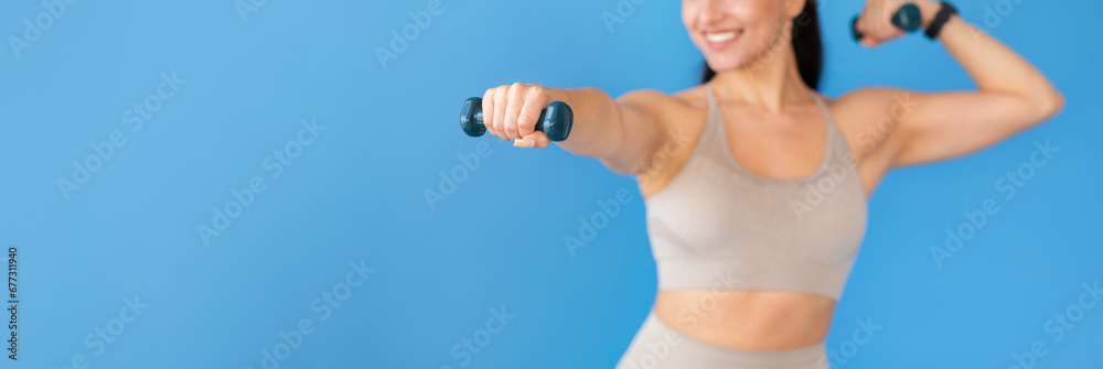Fototapeta premium Cropped of sporty woman doing exercises with dumbbells on blue
