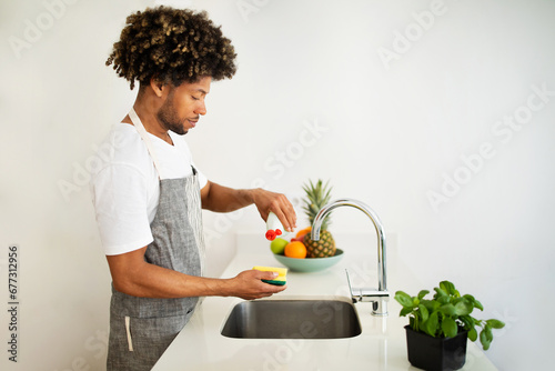 Black man washes dishes at kitchen sink at home