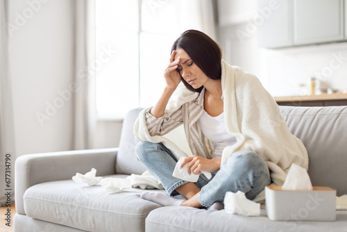 Seasonal Flu Concept. Sick Young Woman Covered In Blanket Sitting On Couch photo
