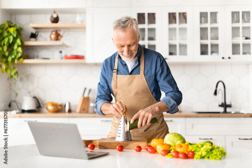 Senior Man In Apron Watching Video Tutorials While Cooking Food In Kitchen Senior Man In Apron Watching Video Tutorials While Cooking Food In Kitchen