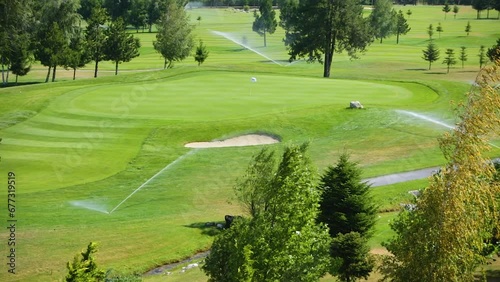 Automatic high-pressure water sprinkler at green golf course watering the grass.