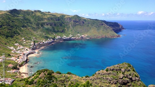 View over the blue ocean and houses on the shore under mountains on a sunny day in Azores, Portugal