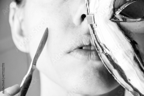 A surgical scalpel is in the hands of a girl next to her face, and a plastic mask covers her face, beauty and fashion photo
