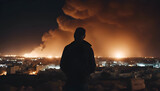 A man in a hood looks at the city at night. Smoke from a chimney.