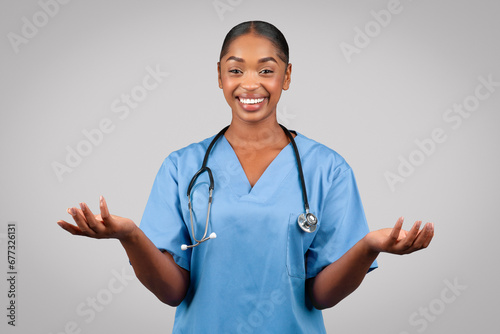 Positive millennial black doctor surgeon, nurse in blue uniform, spread hands to sides