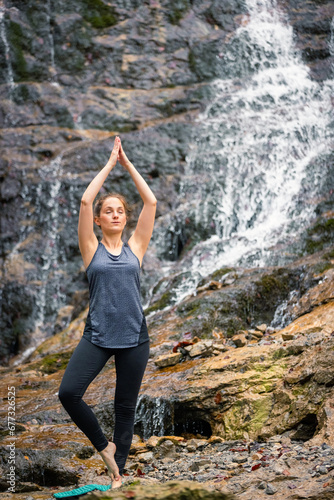 Fit young woman practicing yoga in beautiful waterfall scenery. Concepts of holistic experience  people and nature connection.