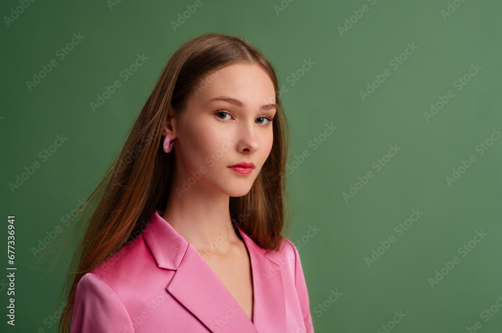 Fototapeta premium Fashionable beautiful confident woman wearing trendy pink satin suit blazer, hoop earrings, posing on green background. Fashion, beauty studio close up portrait. Copy, empty space for text