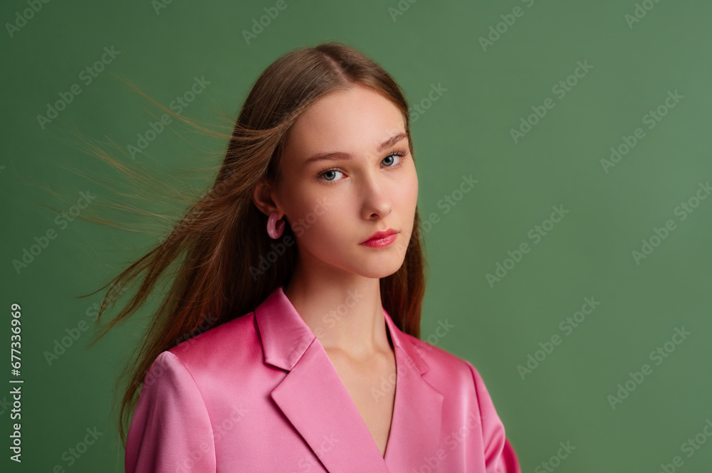 Fashionable beautiful confident woman wearing trendy pink satin suit blazer, hoop earrings, posing on green background. Fashion, beauty studio close up portrait. Copy, empty space for text Fashionable beautiful confident woman wearing trendy pink satin suit blazer, hoop earrings, posing on green background. Fashion, beauty studio close up portrait. Copy, empty space for text