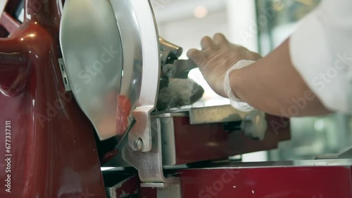Closeup of human hands cutting salami with meat slicer