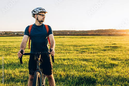Fototapeta Naklejka Na Ścianę i Meble -  Mountain biker having a stop on the beautiful sunset meadow. Healthy lifestyle and outdoor adventure concept