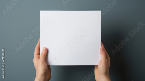 Female hands holding a blank white paper sheet on a gray background.