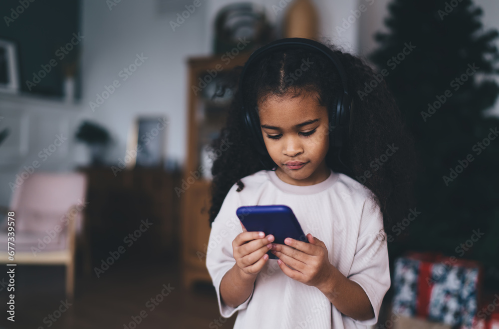 Adorable focused black girl using smartphone at home