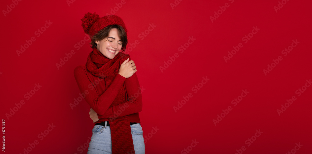 Big banner photo of cheerful young woman presenting seasonal winter promotional offer at red copy space. Cute brunette lady in red winter scarf, sweater and hat. New year and christmas Big banner photo of cheerful young woman presenting seasonal winter promotional offer at red copy space. Cute brunette lady in red winter scarf, sweater and hat. New year and christmas