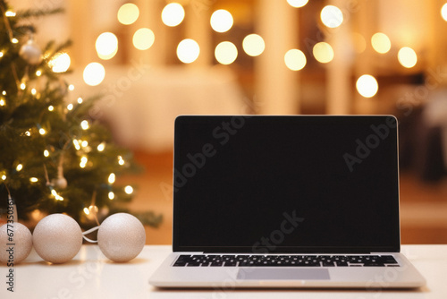 Laptop with blank screen on table in front of christmas tree.