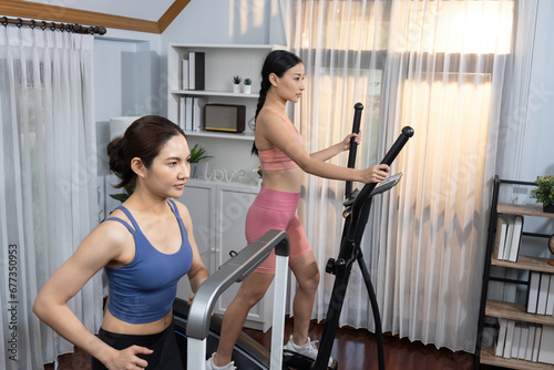 Energetic and strong athletic asian woman running on elliptical running machine at home with workout buddy or trainer. Pursuit of fit physique and commitment to healthy lifestyle. Vigorous