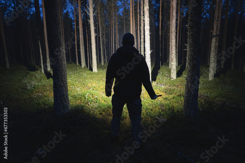 Silhouette of a man with a knife and a flashlight in a dark forest.