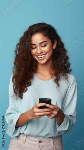 Radiant woman with dark skin in a blue shirt, beaming at her phone against a vivid blue backdrop, exuding joy