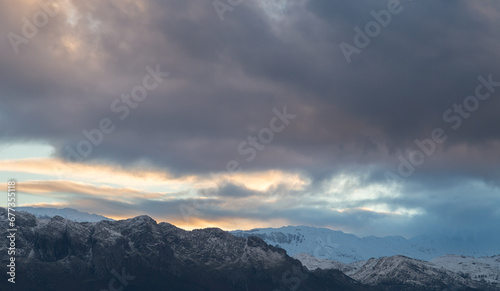 Obraz na płótnie mountain during sunset with snow on the summit and a storm approaching them. w salonie