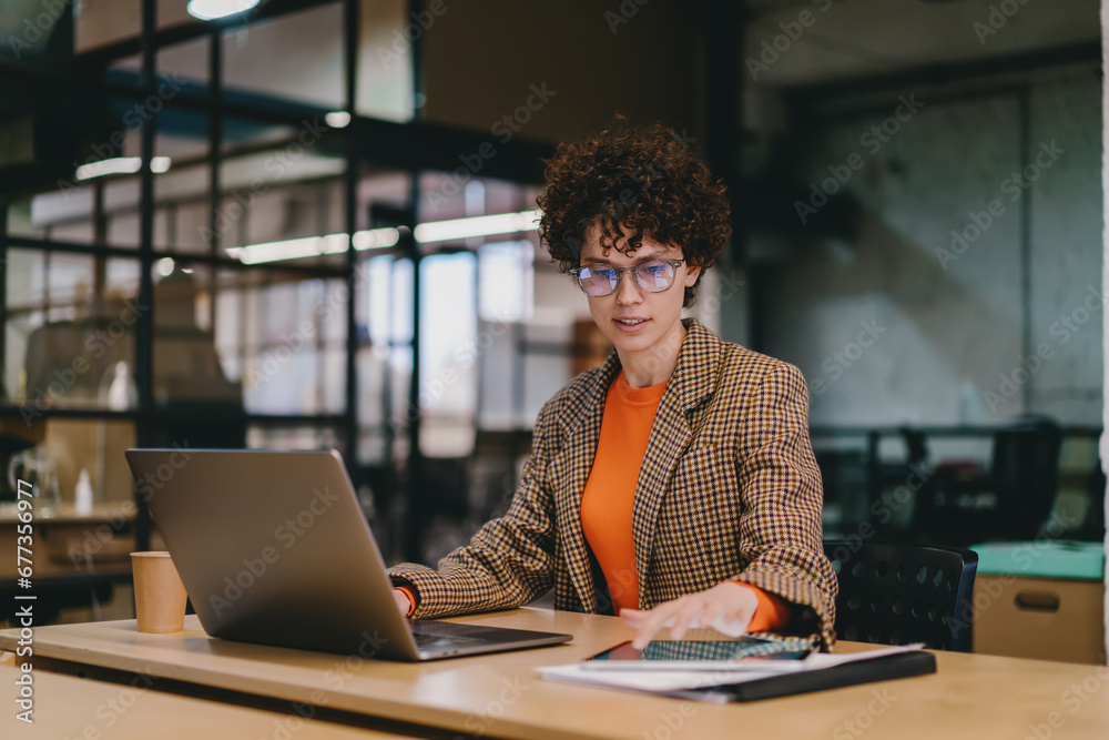 Focused young woman using laptop while sitting at table in office Focused young woman using laptop while sitting at table in office