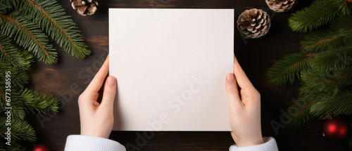 Top view of woman holding blank sheet of paper near christmas decorations on wooden table.