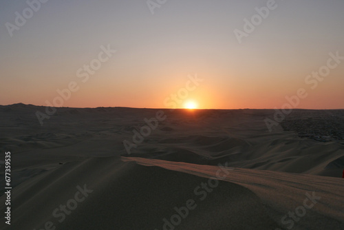 Last rays of orange sunet reflecting on a dune in the foreground. Location: Huacachina, Peru