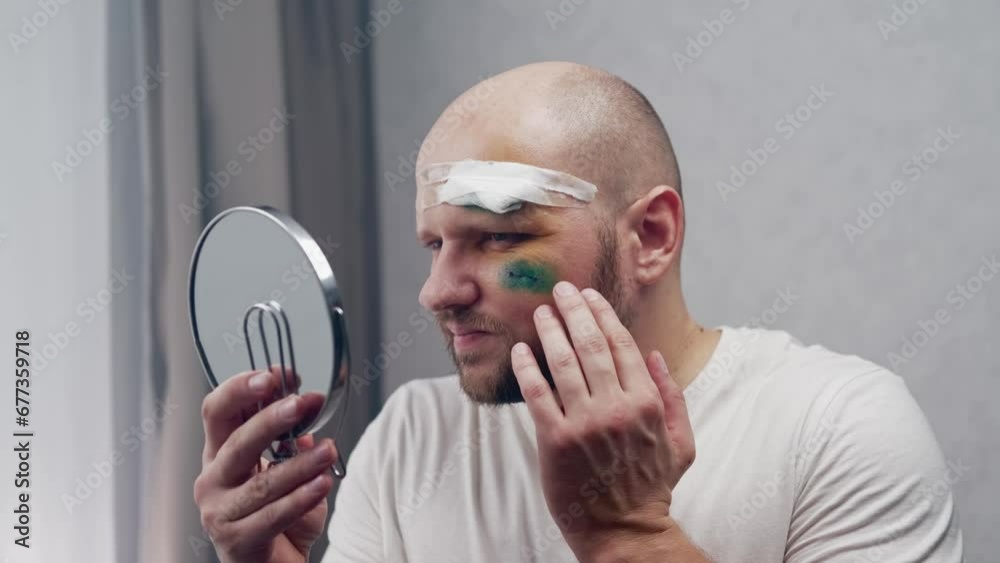 A wounded man with a stitched incision and a medical bandage on his forehead looks in the mirror, touches the wounds and sobs in pain. Concept consequences of a car accident