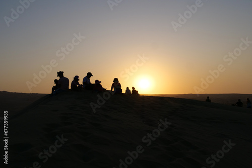 Black silhouettes of a group of people sitting on a dune at Huacachina oasis town  waiting for the sunset