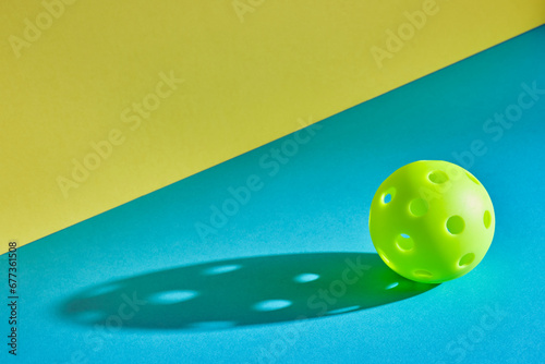 green pickleball ball with shadow on a blue surface with a yellow wall next to it