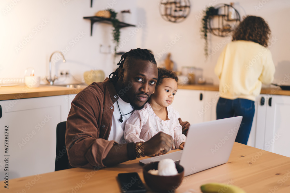 Pensive black father and daughter using laptop while sitting at dining table in kitchen Pensive black father and daughter using laptop while sitting at dining table in kitchen