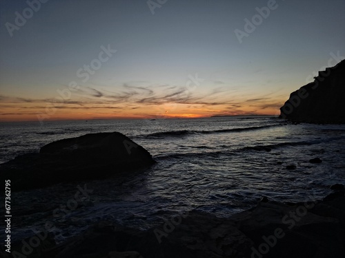 Rocky beach with stones by splashing sea under sunset orange sky
