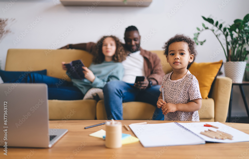 Adorable little girl standing by table with open notebook and stationery while looking at camera Adorable little girl standing by table with open notebook and stationery while looking at camera
