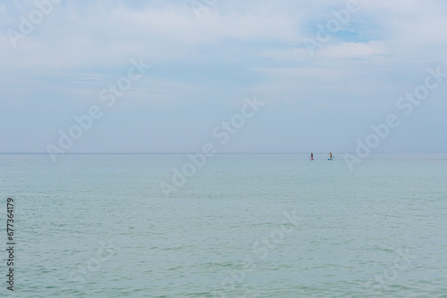 sea and blue sky of identical hue, on the right side two people practicing padlle. Atlantic ocean on the Algarve coast of Portugal