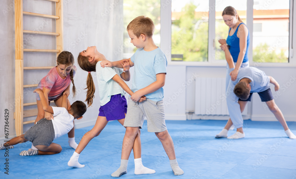 Obraz premium Children boy and girl partner in sparring practice technique practicing basic attacking movements and maneuvers. Class self-defense training in presence of experienced instructor