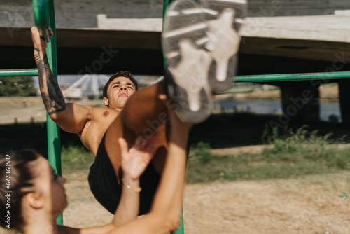 Fitness friends warm up, challenging their bodies with pull ups on metal bars in a sunny park. They demonstrate the positive results of a healthy lifestyle and persistence in outdoor exercise.