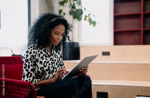Concentrated Black female financial trader in leopard print blouse analyzing real-time data on tablet in a stylish office, with a touch of executive flair