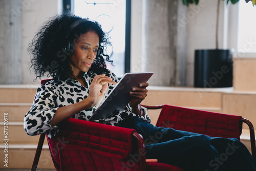 Diligent Black female market analyst in fashion-forward leopard print top  deeply engrossed in financial forecasting on a tablet  in a chic office setting