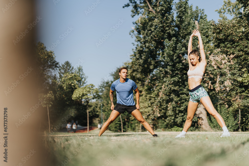 Fit couple stretching and warming up in a park for their outdoor workout. Friends motivating each other for a healthy lifestyle. Recreational sports and sportsmanship spirit captured. Fit couple stretching and warming up in a park for their outdoor workout. Friends motivating each other for a healthy lifestyle. Recreational sports and sportsmanship spirit captured.