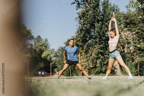 Fit couple stretching and warming up in a park for their outdoor workout. Friends motivating each other for a healthy lifestyle. Recreational sports and sportsmanship spirit captured.