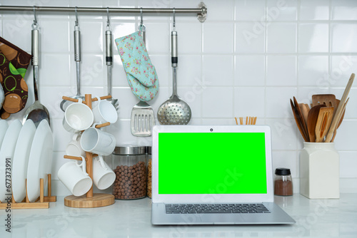 Mockup of laptop computer with empty green screen sugar, spices in glass jars eggs, vegetable,tomato and a whisk on the kitchen on white table. Flat lay. Concept of food preparation, on background.