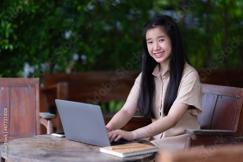 Happy of Young asian teen girl college student using laptop computer writing on pc working from at the cafe.Online education, elearning concept,freelance people businessfemale