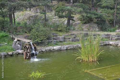 Old traditional watermill on a pond at the Namsangol Hanok Village, Seoul, South Korea © Wirestock