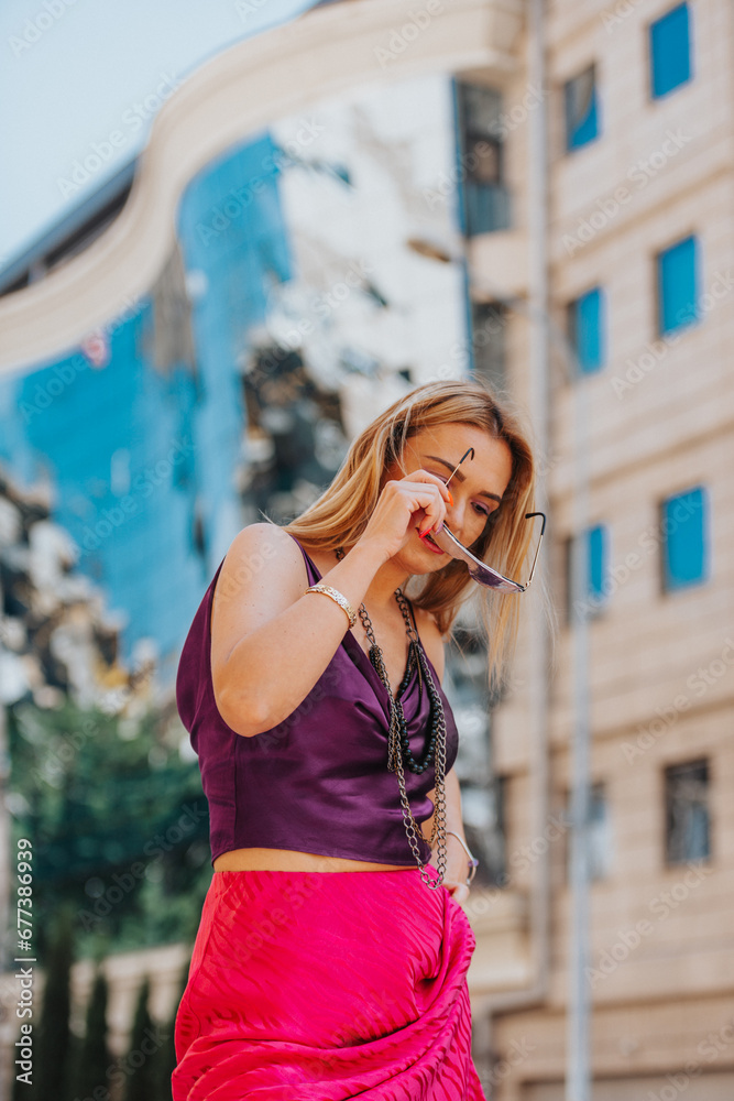 An elegant, attractive lady confidently poses in trendy street fashion against a modern city backdrop. Vibrant shades of pink and purple add a stylish touch to her well-dressed outfit.