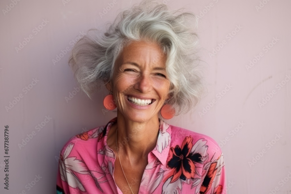 Portrait of a happy senior woman smiling against a pink wall.