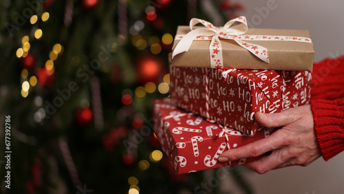 Female hands in red sweater hold Christmas New Year gift box on background of Christmas tree.Giving gifts for holidays.Christmas holidays celebration concept,gifts for family,friends.Winter banner