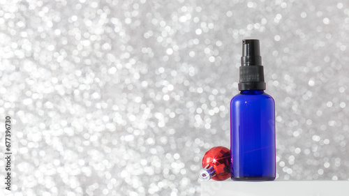 Dispenser with serum or oil for youthful skin on a silver background with a Christmas ball. Skin care 